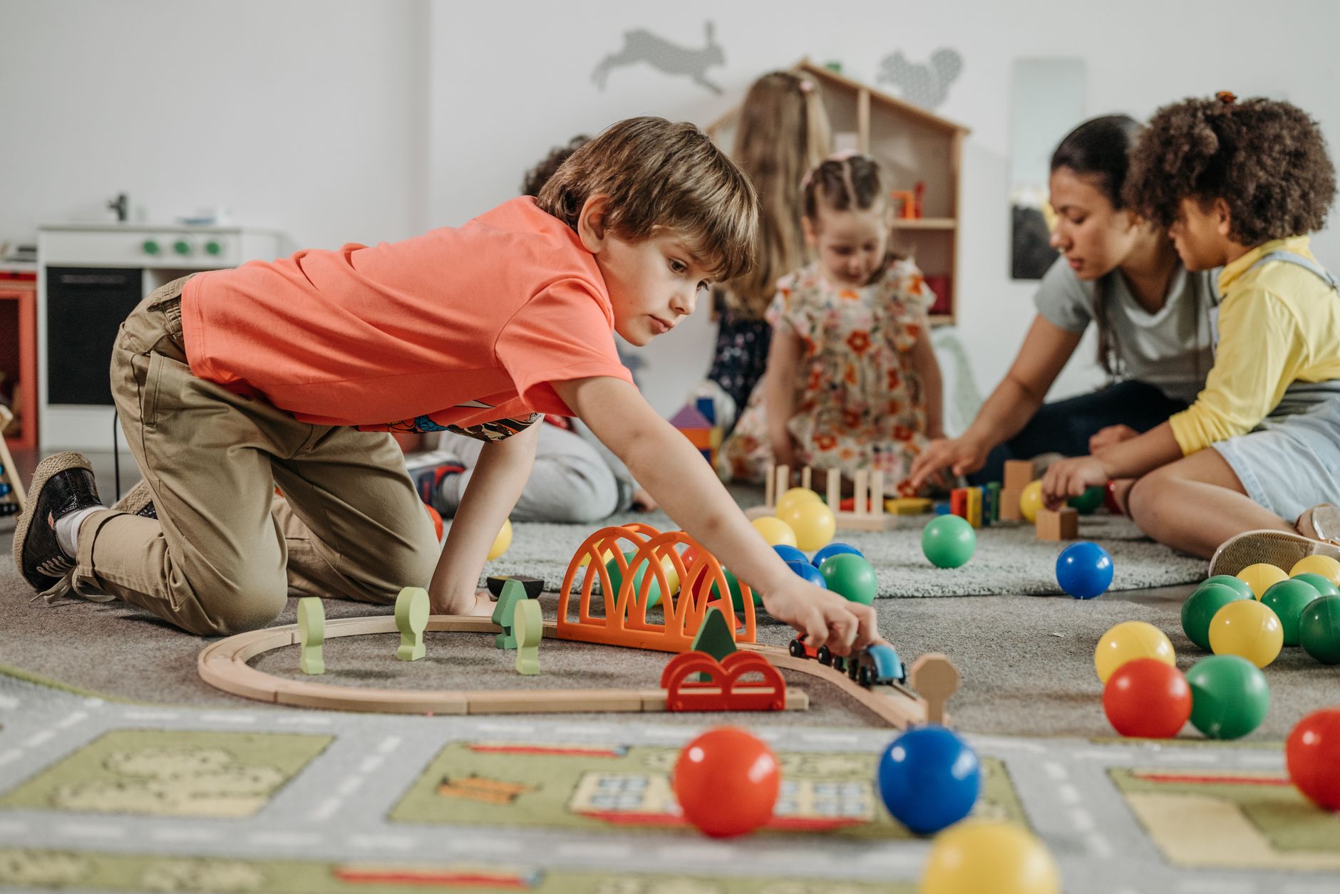 Children playing with toys alongside an adult in a nursery room.
